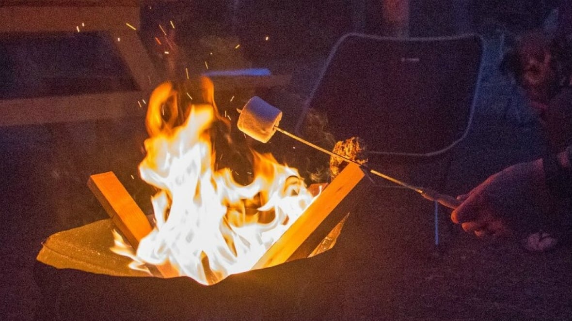 A marshmallow is seen roasting over a campfire. A picnic bench is seen in the distance. As is a camping chair.