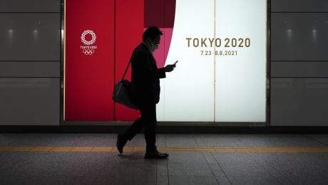 A man wearing a protective mask to help curb the spread of the coronavirus walks near advertisement for Tokyo 2020 Olympics at an underpass Tuesday, April 6, 2021, in Tokyo. Japanese news agency Kyodo on Sunday said Olympic organizers are working to secure 300 rooms in a hotel near the Athletes' Village for any athletes that come down with symptoms of COVID-19. Virus Outbreak Japan Olympics