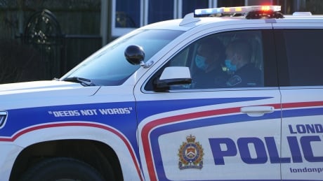 Two police officers wear surgical masks inside their vehicle at the scene of a routine traffic stop in London, Ont. covid london police