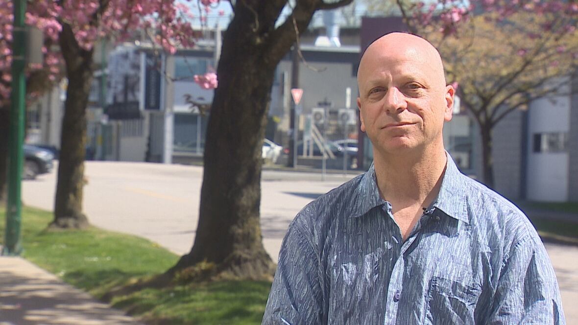bald man wears blue button up shirt next to a tree with pink flowers