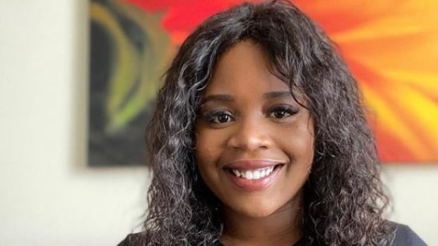 A smiling woman with black curly hair wears a shirt that reads 'Mind Your Own Plate.'