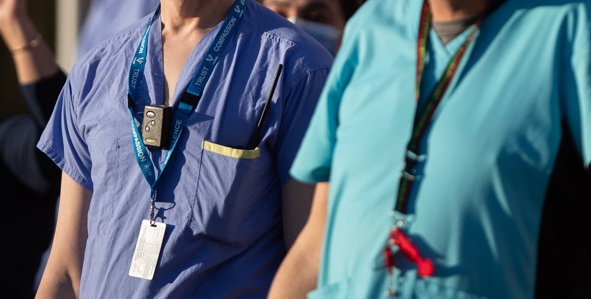 The torsos of two medical workers wearing scrubs, one dark blue, the other teal.