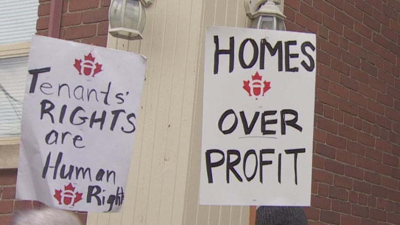 Tenants at a protest hold signs saying "tenants rights are human rights" and "homes over profits."