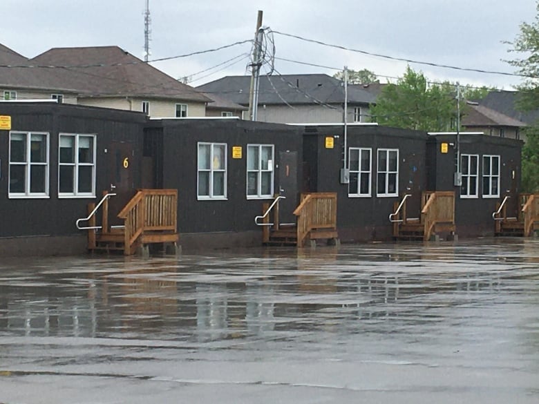 A quartet of brown, individual portable classrooms sit on a paved portion of a school yard on a rainy day.