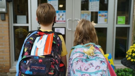 Children line up on the first day of school in London, Ontario.
See two students outside front door, shot from behind. covid london school
