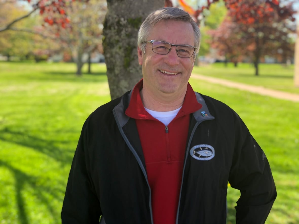 Man stands outdoors infront of a tree smiling at the camera. 