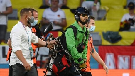 A paraglider, who flew inside the stadium sporting a message from environmental action group Greenpeace, is escorted by security after landing on the pitch during a match between France and Germany at Euro 2020 on Tuesday. Protest-Greenpeace-150621