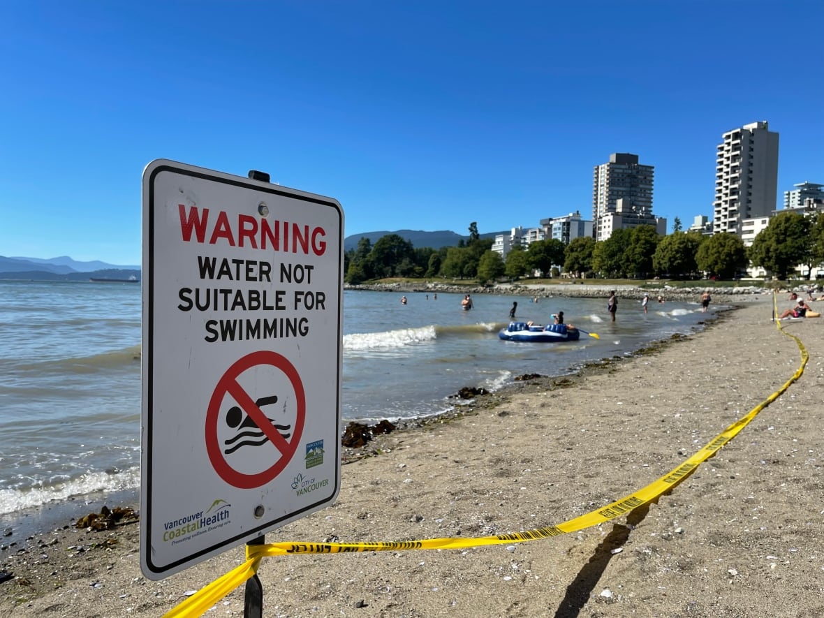 A sign that says "warning, not suitable for swimming" in front of English Bay beach in Vancouver.