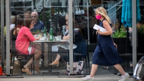 Diners are pictured eating a restaurant in downtown Vancouver, British Columbia as a pedestrian passes wearing a face mask to reduce, and protect against, the spread of COVID-19 on Tuesday, June 22, 2021. COVID-19 DAILY LIFE