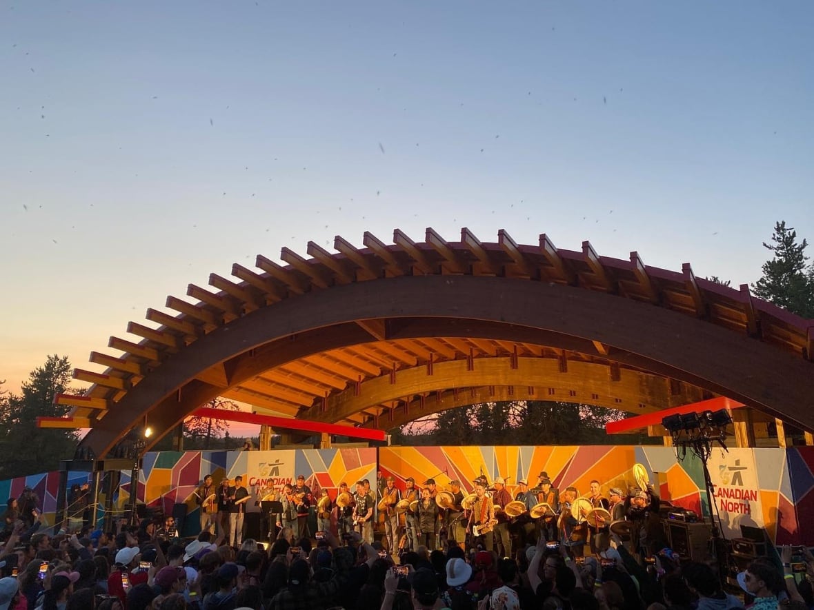 Musicians perform on an outdoor stage before a crowd of people.