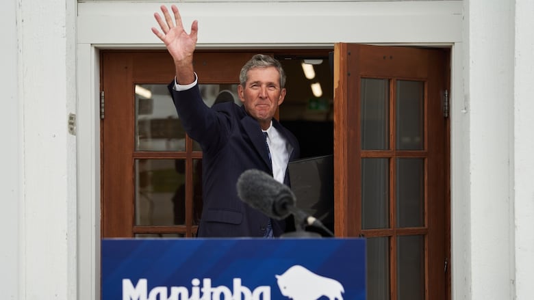 A man waves in front of a podium that says "Manitoba."