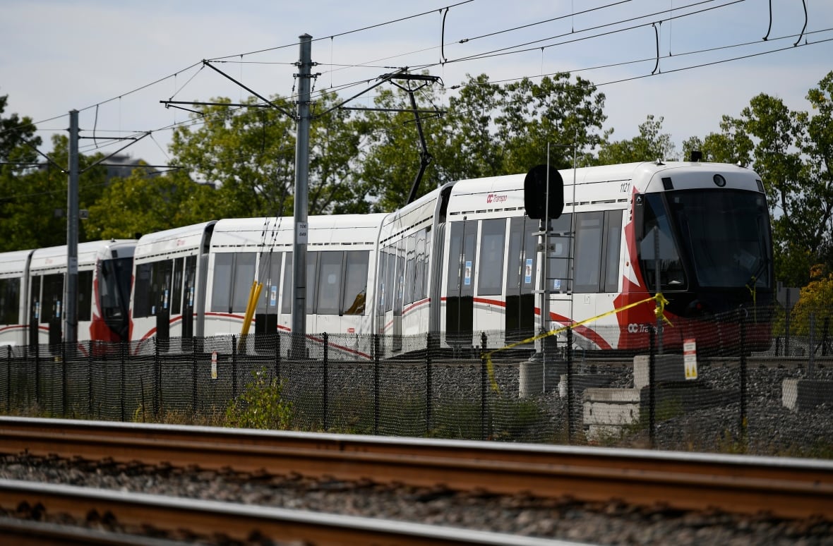 A red and white light rail train rests on the tracks after a minor derailment.