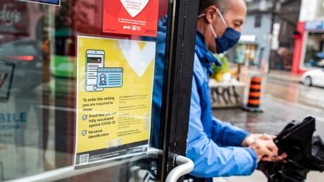 A patron leaves a fast food restaurant on Queen Street in Toronto, past a sign displaying proof of vaccination information on Sept. 22, 2021. Starting today, patrons of Ontario dine-in restaurants, nightclubs, gyms, sports facilities and other venues must present a receipt of full vaccination along with government identification. Vaccine Passport Toronto Restaurant