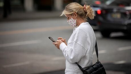 A person looks at their cellphone while wearing a mask to reduce their risk of spreading or contracting COVID-19 in downtown Vancouver, British Columbia on Monday, Oct. 4, 2021. COVID-19 DAILY LIFE