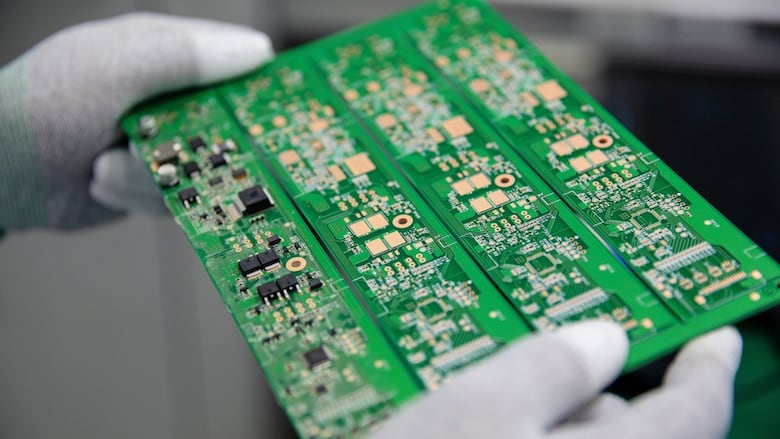 White gloved hands hold a large green circuit board with semiconductors