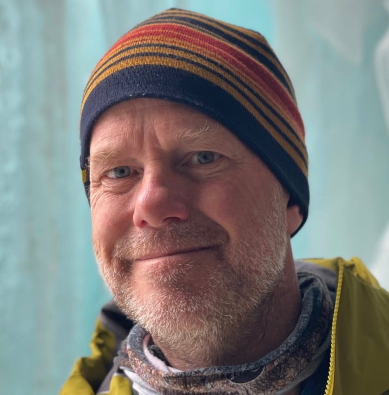 A man wearing a toque outdoors smiles at the camera