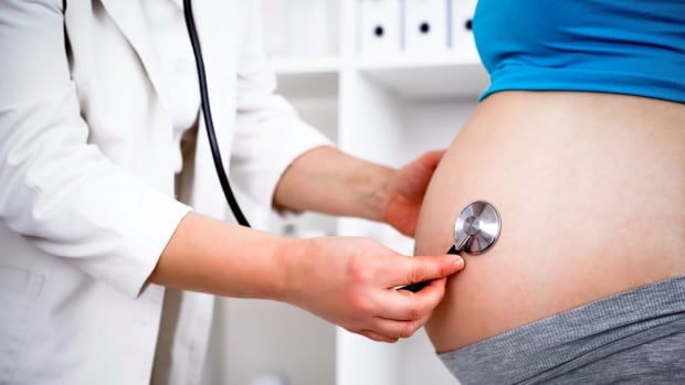 A health-care provider holds a stethoscope up to the abdomen of a pregnant patient.