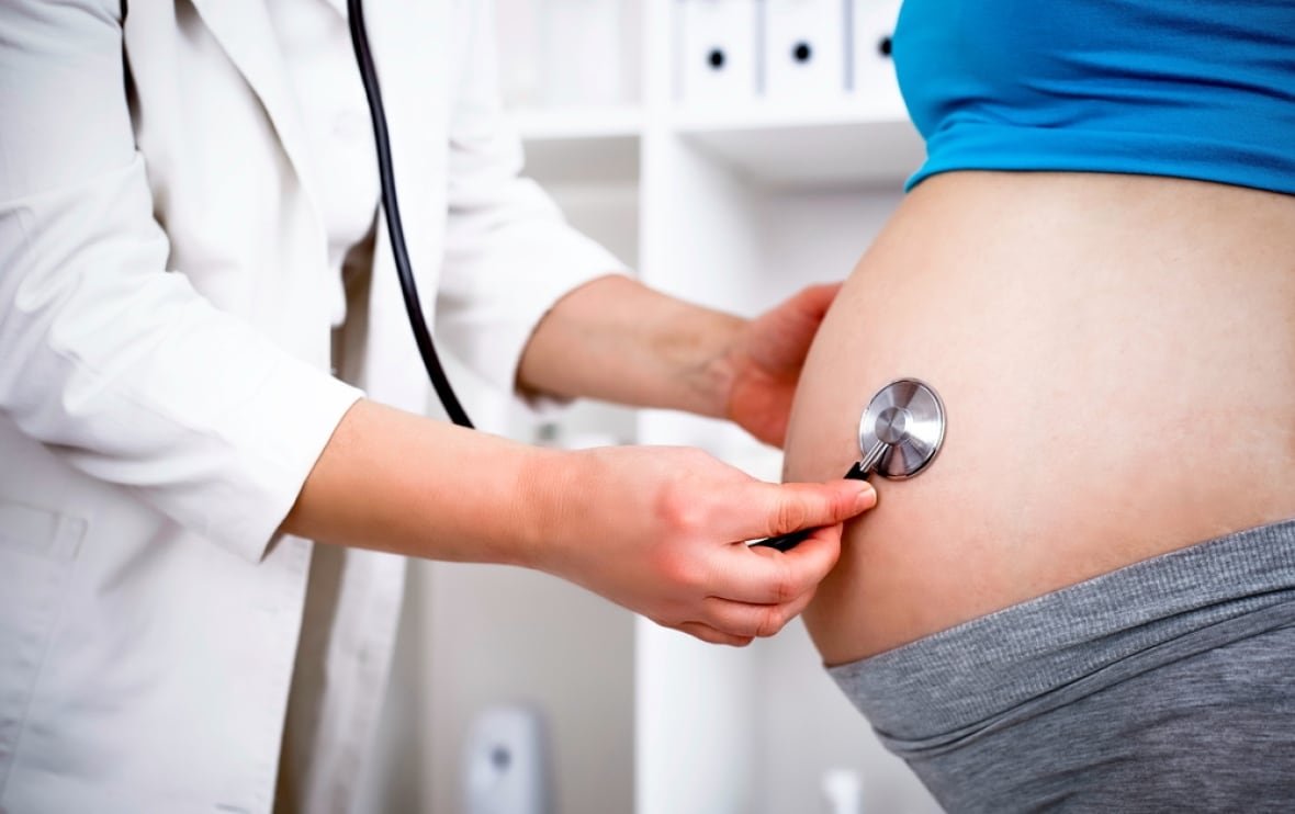 A health-care provider holds a stethoscope up to the abdomen of a pregnant patient.