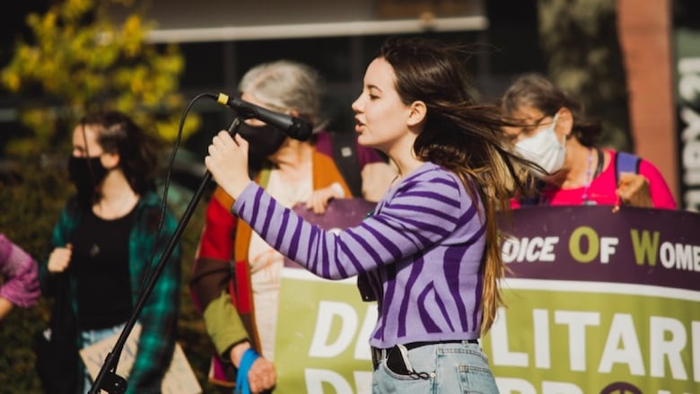 A teenage girl speaks into a microphone at a rally.