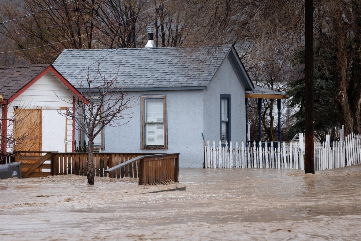 Flooding sweeps past a house with a white picket fence