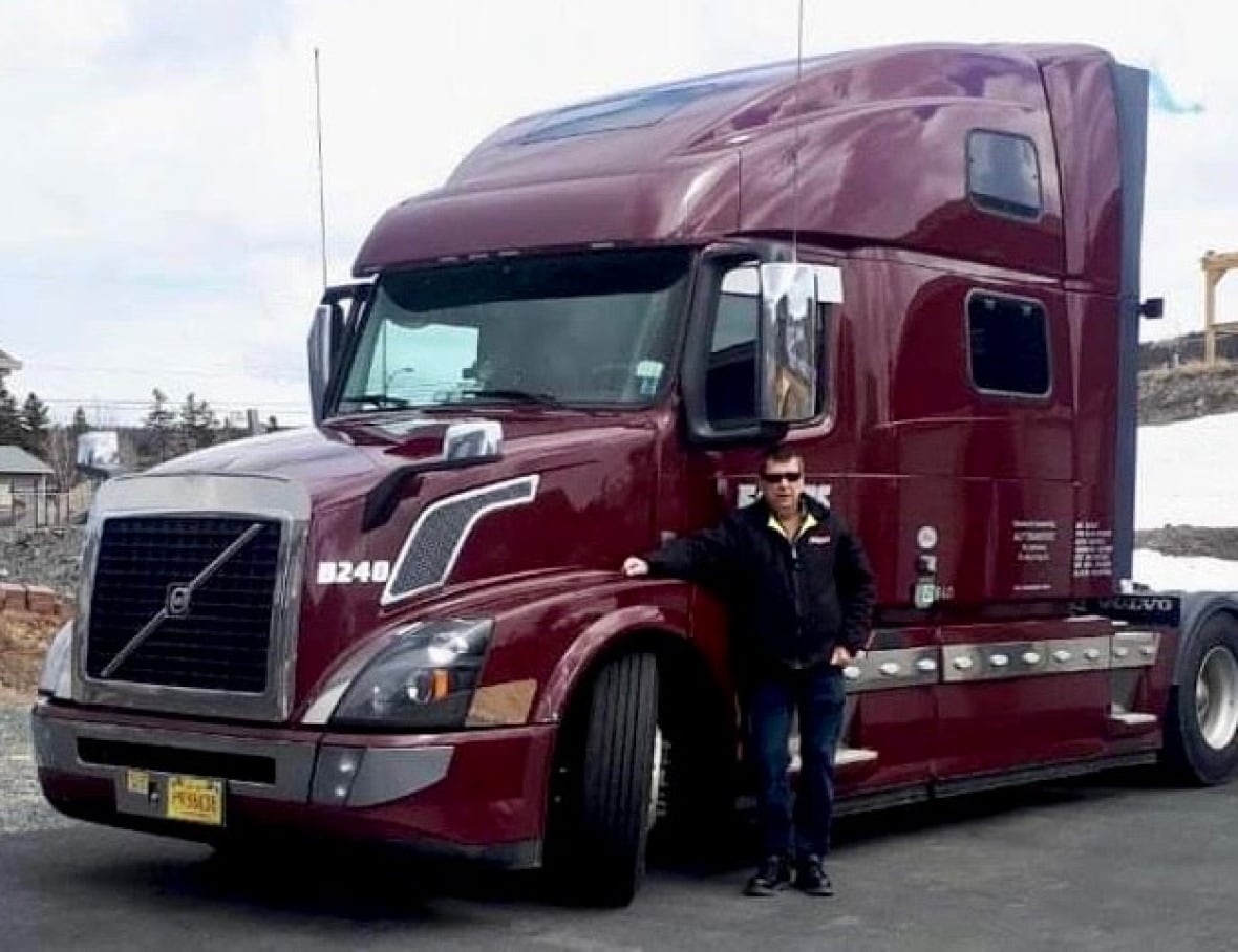 A man stands in front of a maroon transport truck.