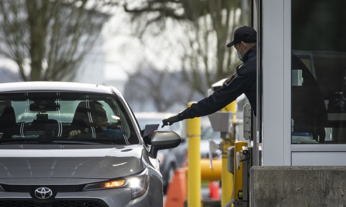 An officer at a border crossing extends to take out someone's documents from the window.