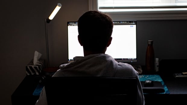 A teen sits in front of a computer in the dark.