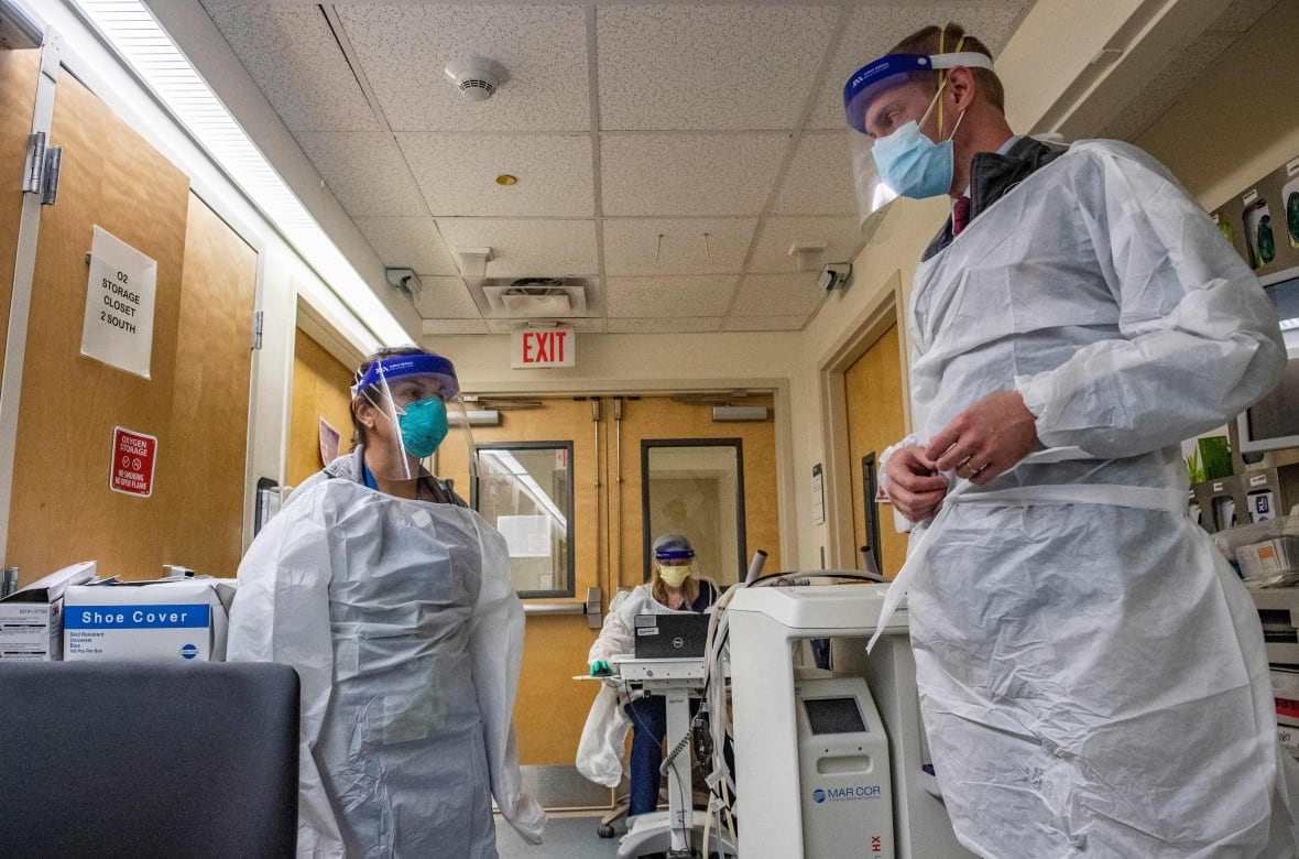 a man and a woman in PPE talk to eachother in the hallway of a hospital