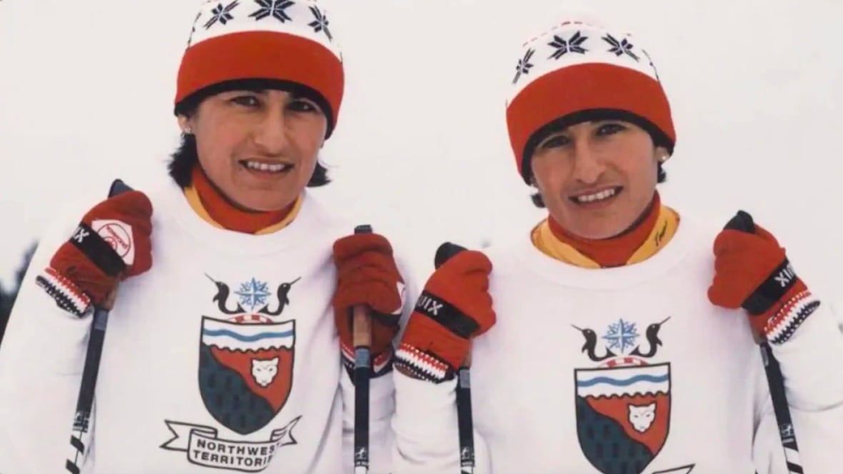 Two twin women are shown outfitted to compete in cross-country skiing.