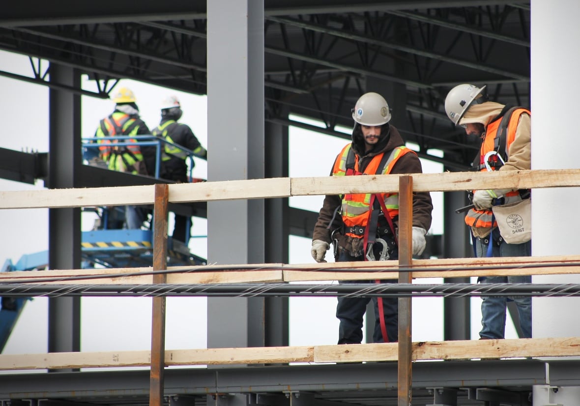 Construction workers in fluorescent orange vests stand on scaffolding while putting up a new building.