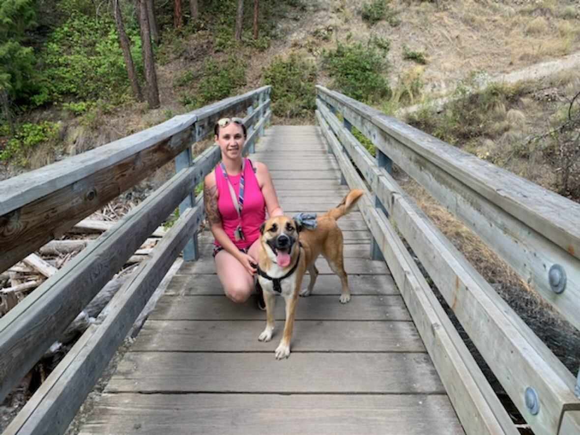 A woman poses next to a dog. They're both standing on a bridge.
