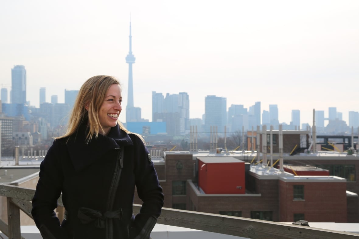 A woman stands in front of the Toronto skyline.