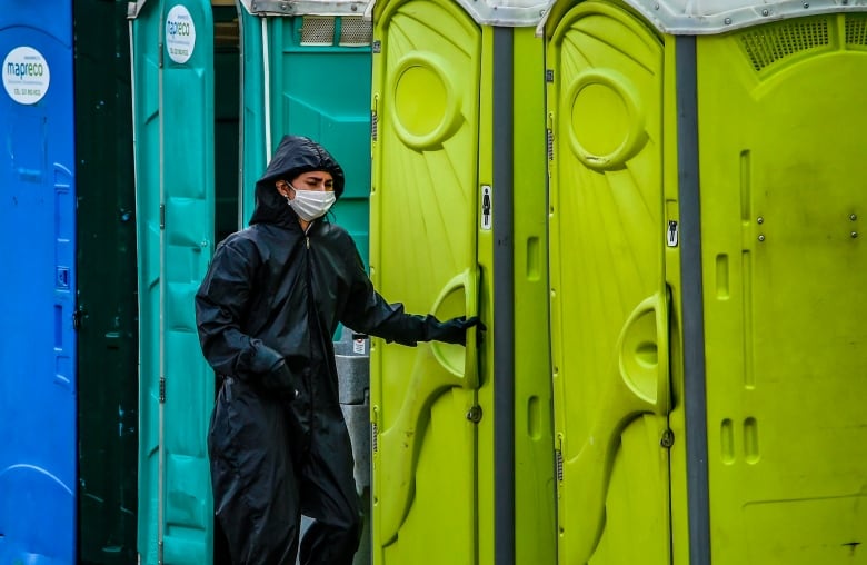 A woman wearing a mask stands outside public toilets.