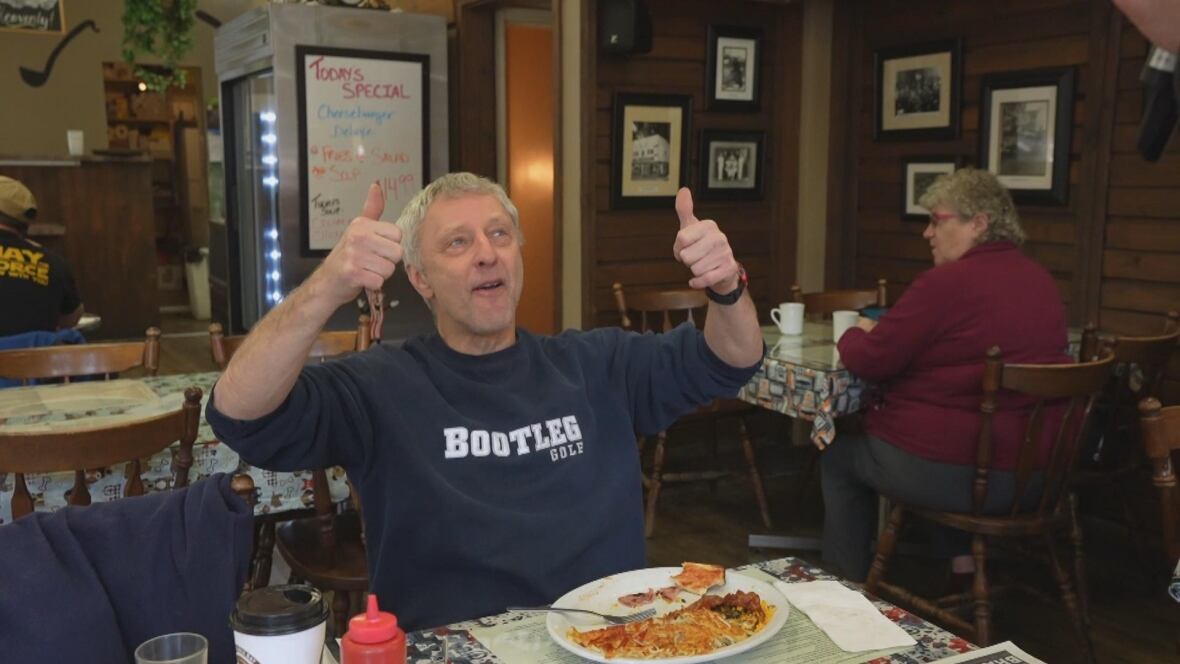 A man gives two thumbs up, seated inside a pub.