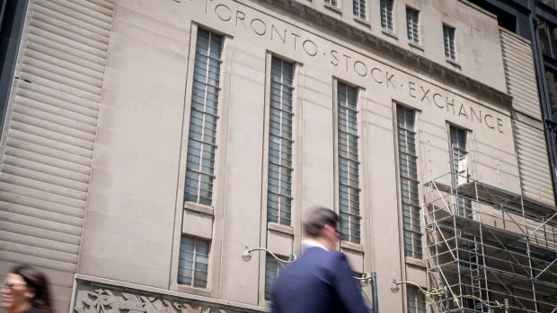 a man in a suit walks in front of a big stone building with the words "toronto stock exchange" etched into it