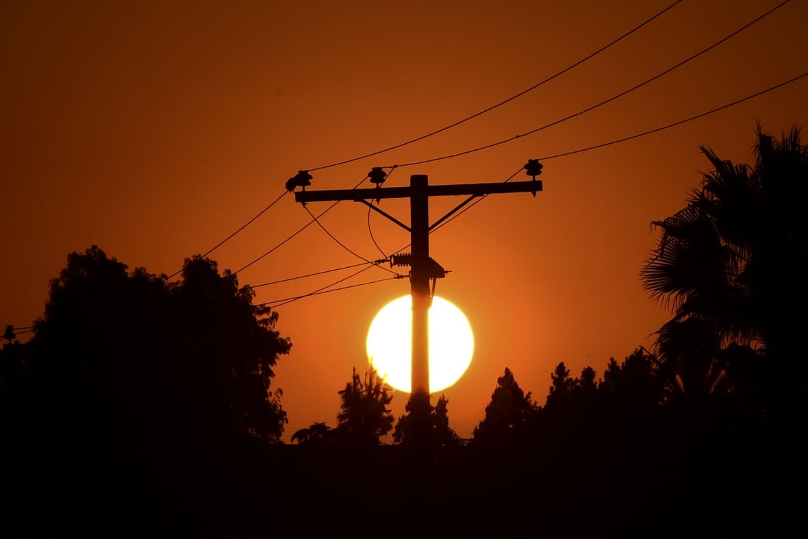 The sun sets behind the dark silhouette of power lines in an orange sky