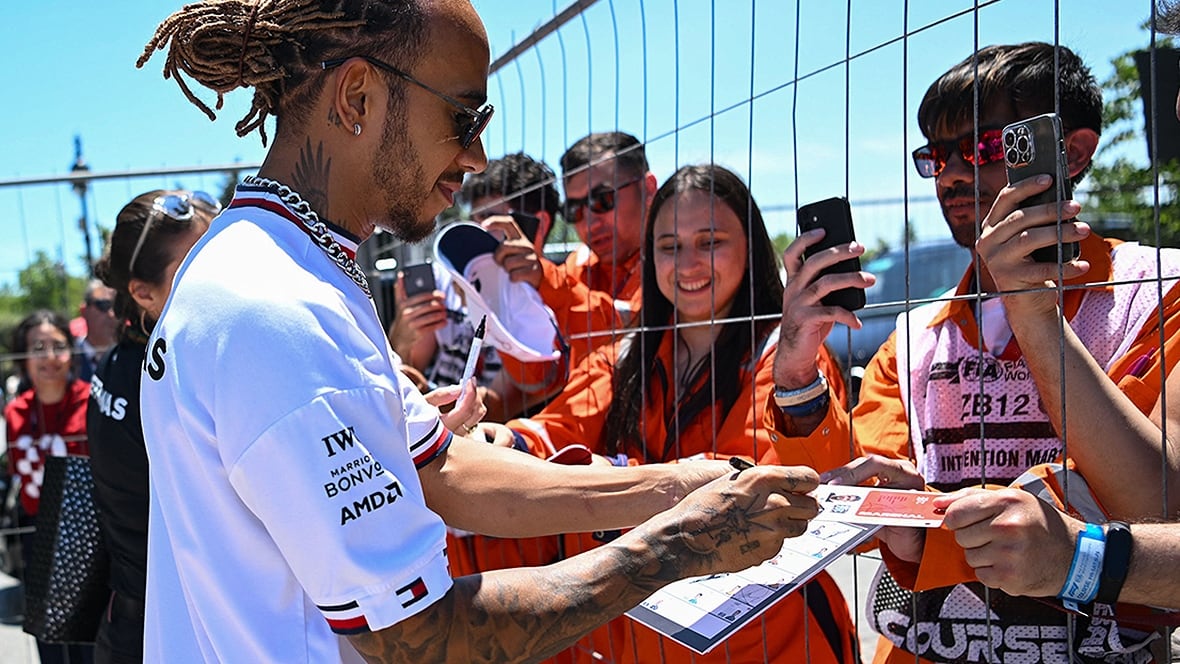 Lewis Hamilton signing posters for fans through a metal gate.