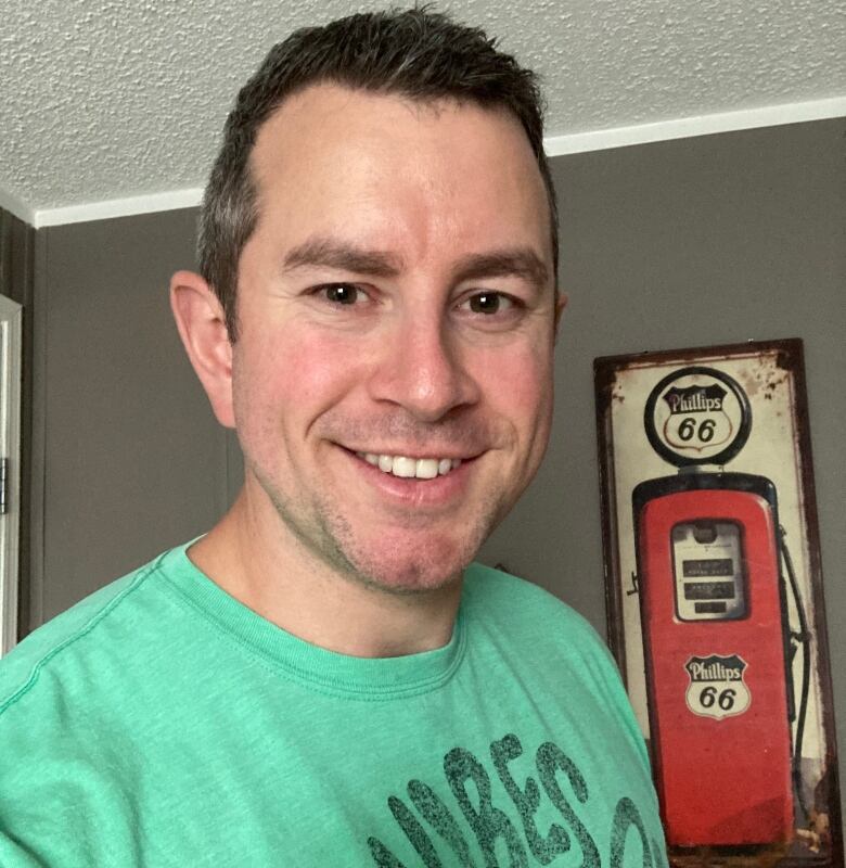 A man wearing a green T-shirt smiles while looking at the camera.