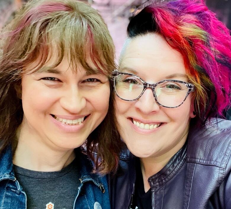 Two women standing side-by-side and smiling. 