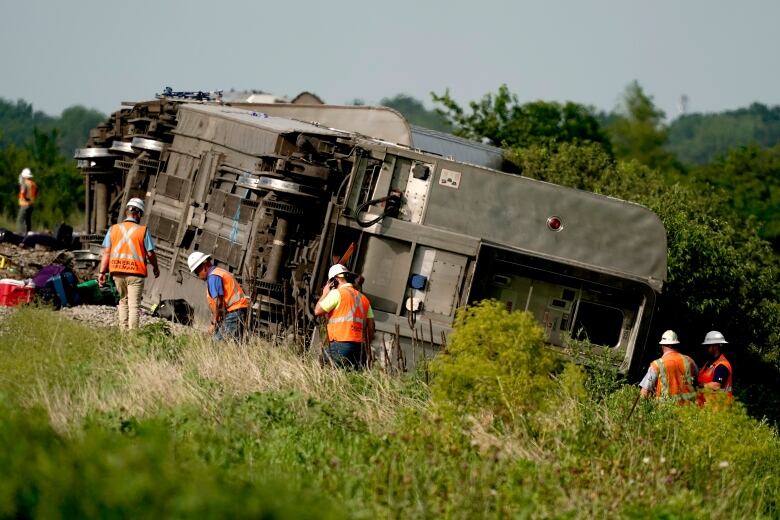 Workers in reflective vests work at the site of a derailed train.