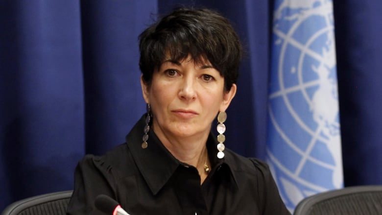 Woman with short, dark hair and dressed in dark clothing with long hanging earrings, sits looking pensive