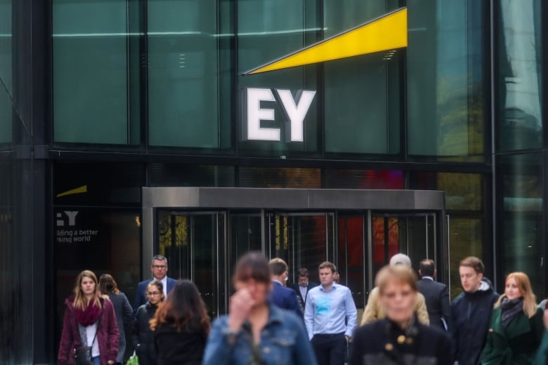 Pedestrians pass in front of the offices of Ernst & Young. A big "EY" is displayed on the glass building.