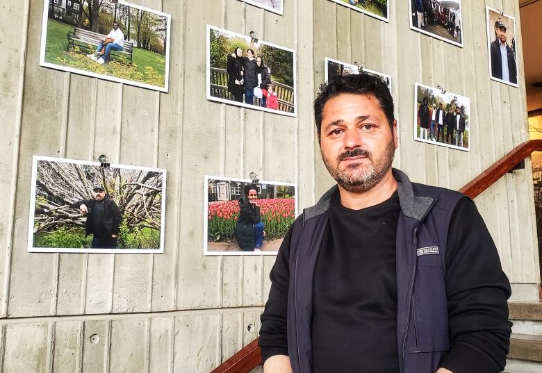 A person stands in front of 10 photos hanging on a concrete wall.