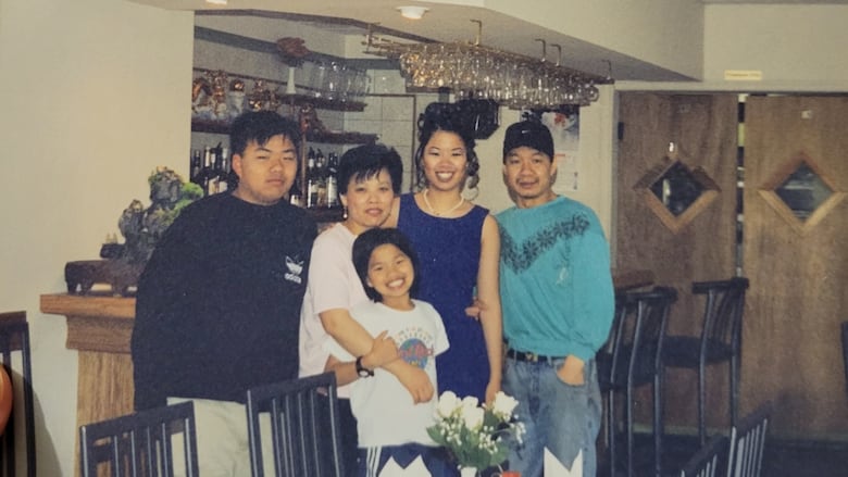 A smiling family of five stands next to a dining table inside a restaurant.  