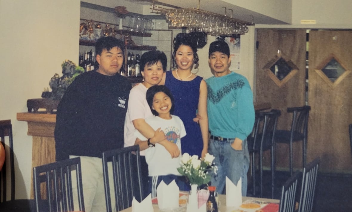 A smiling family of five stands next to a dining table inside a restaurant.  