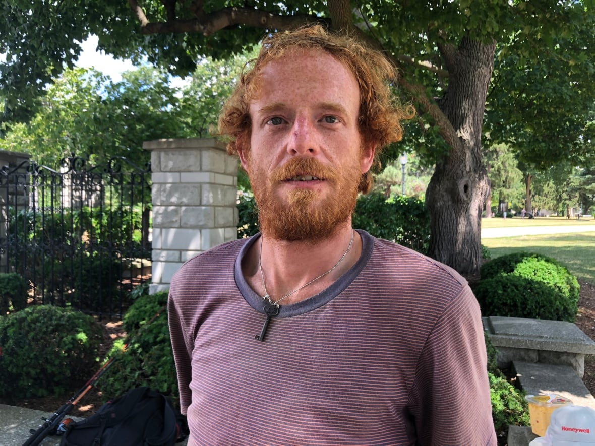 Man looking into camera, he's got a beard and T-shirt, he's standing in a park. 