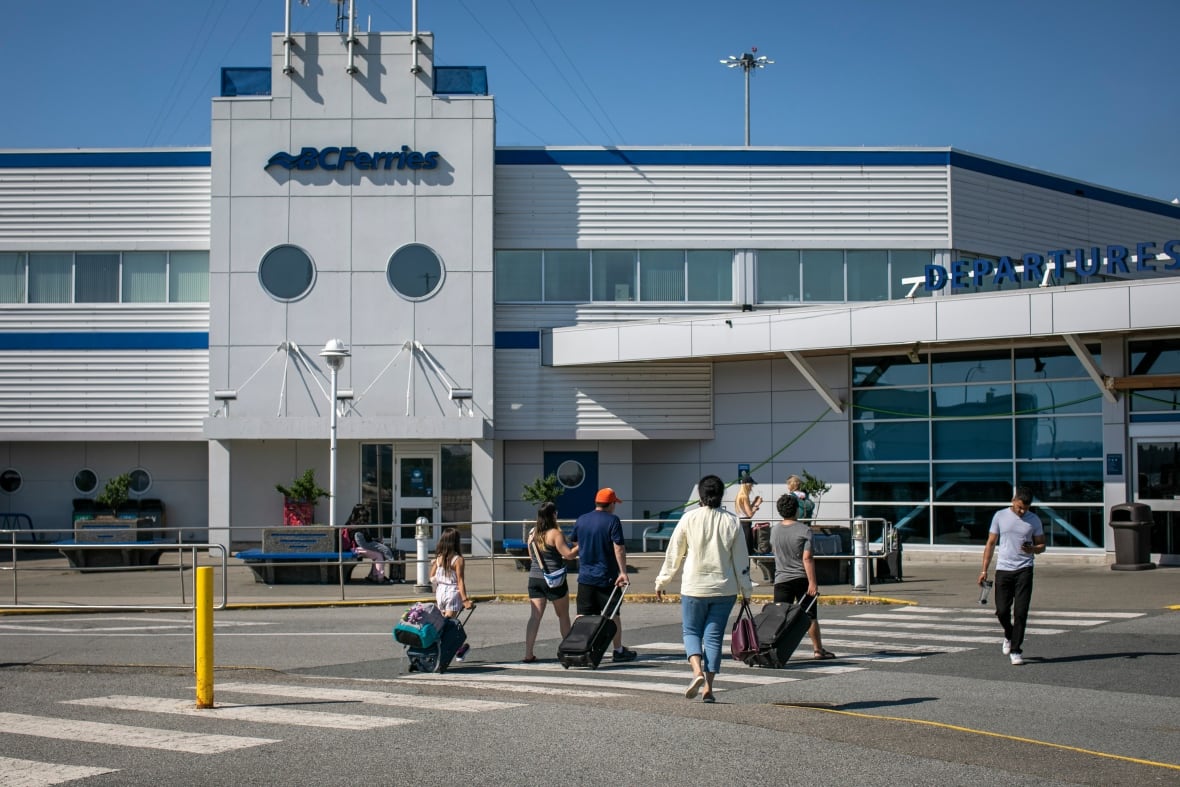 A number of people with luggage approach a B.C. Ferries terminal.