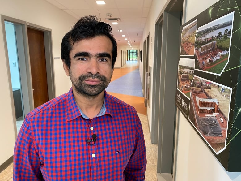 Photo shows Dr. Aitazaz Farooque standing in the hallway of the Canadian Center on Climate Change and Adaptation at UPEI.  On the right wall there are photos of the center in development. 