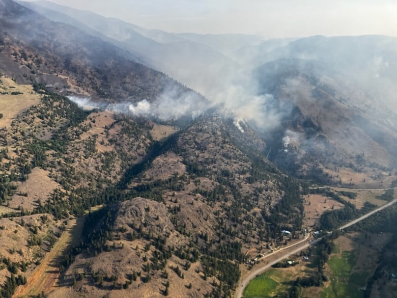 Smoke rises from a rocky hilltop, with a road visible beneath it.