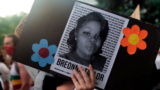 A photograph of a young Black woman pasted on a sign is held by a demonstrator.